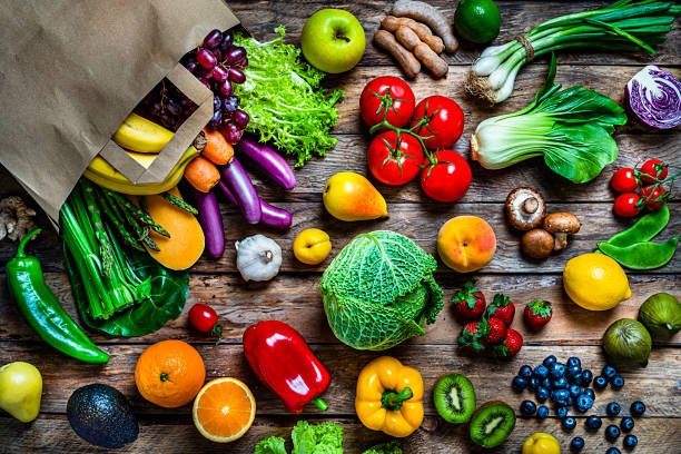 Healthy food: brown paper shopping bag filled with multicolored fresh organic fruits and vegetables shot from above on rustic wooden table. Fruits and vegetables included in the composition are apple, strawberry, banana, kiwi, orange, pear, grape, tamarind, blueberry, peach, lime, lemon, fig, kale, tomatoes, squash, asparagus, potato, celery, eggplant, carrots, lettuce, edible mushrooms, bell peppers, cauliflower, ginger, radish, avocado, onion, chili pepper, corn, among others. High resolution 42Mp studio digital capture taken with SONY A7rII and Zeiss Batis 40mm F2.0 CF lens