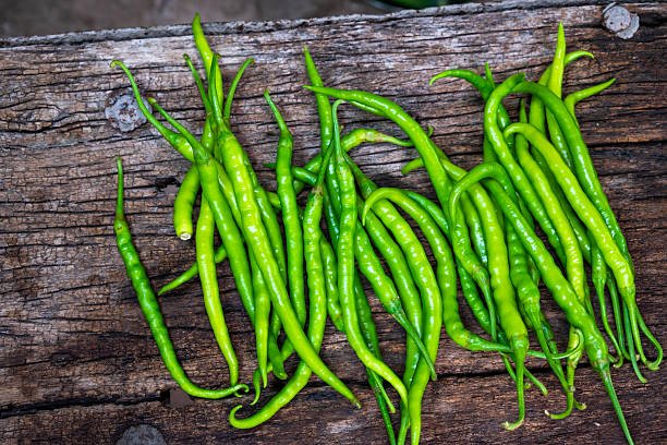 Fresh organic green chili peppers arranged on an old rustic wooden surface. Long, spicy green peppers freshly harvested from the farm.