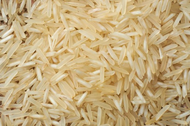 close-up macro view of raw basmati rice grains, pile of creamy white color grainy background in full frame, food wallpaper or backdrop